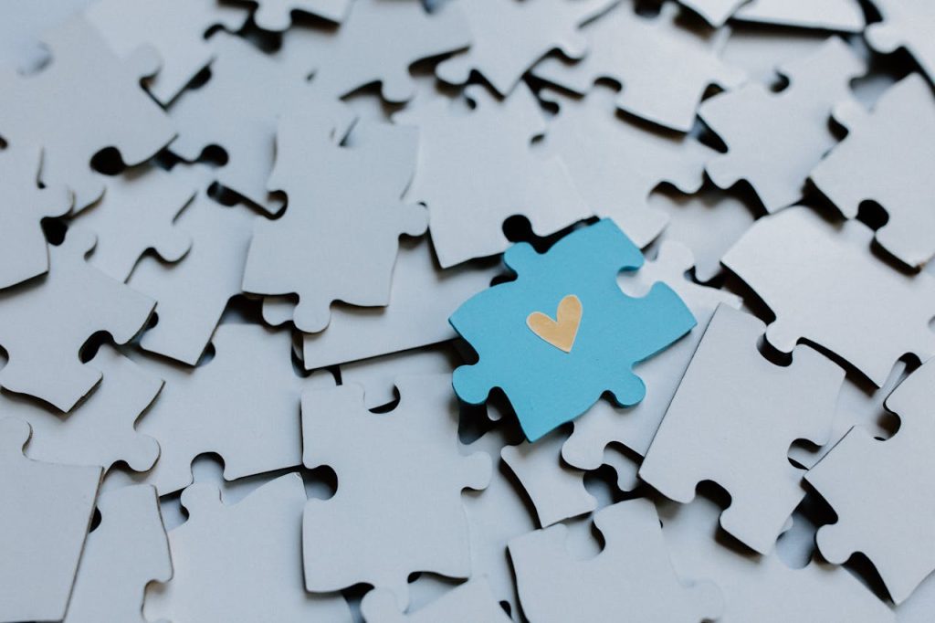 A single blue puzzle piece with a heart amid scattered pieces, symbolizing connection.